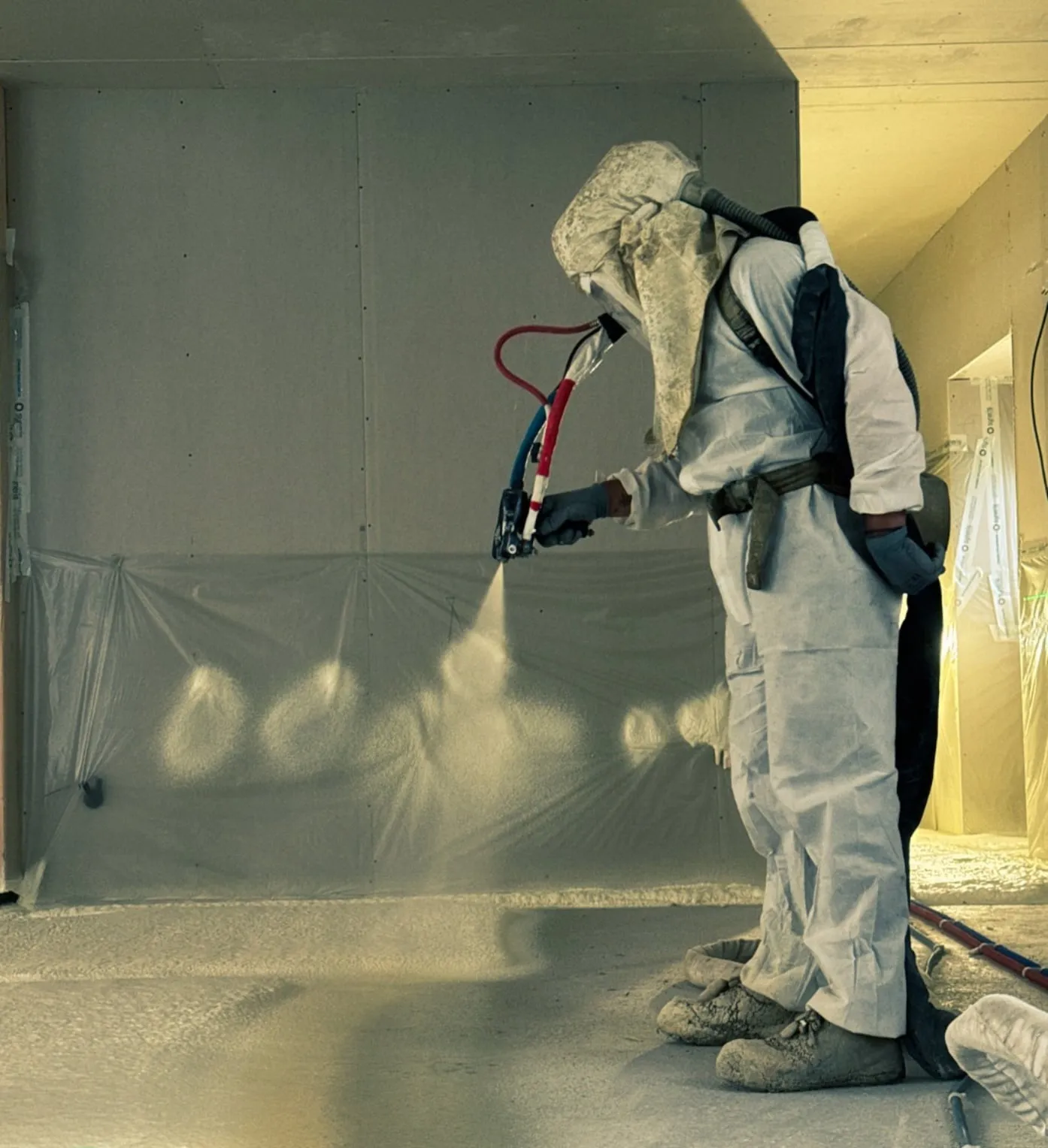 Applicateur en projection polyuréthane sur mur, lumière naturelle dorée, chantier en production · Pérouse · Isolatech