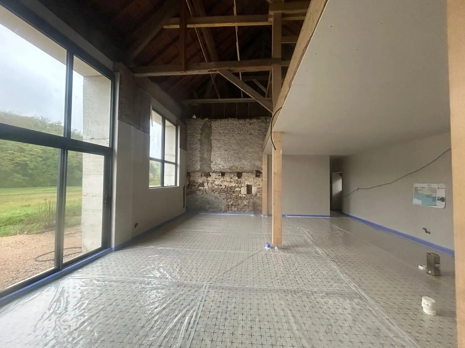 Grande pièce loft avec charpente bois et mur pierre apparente après isolation polyuréthane des sols · chantier Isolatech